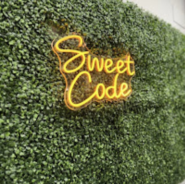 Sweet Code neon sign on a green leaf wall inside the shop